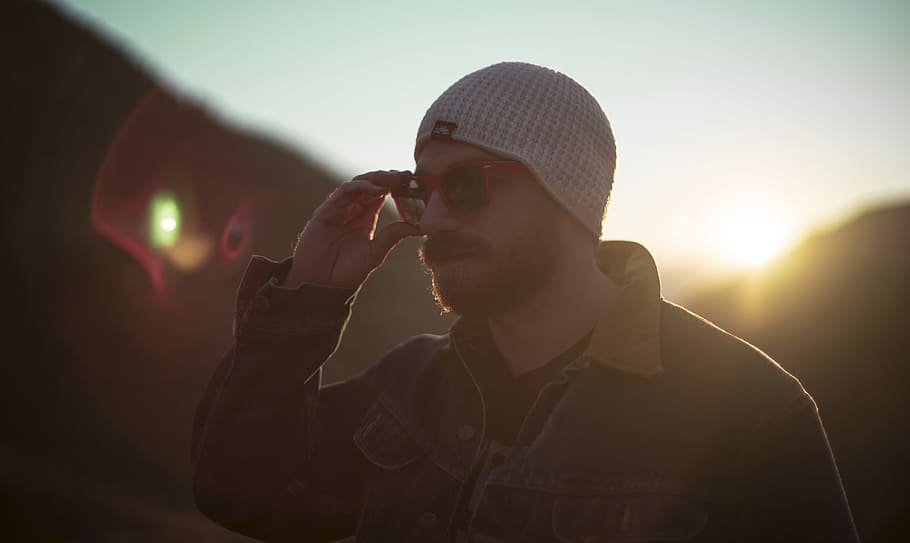 woman holding his sunglasses standing near mountain, man wearing white knit hat holding sunglasses HD wallpaper