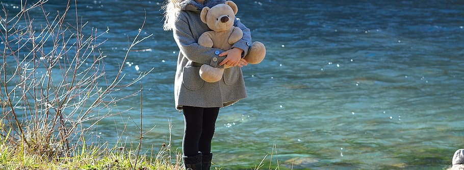 person hugging brown bear plush toy near body of water during daytime HD wallpaper