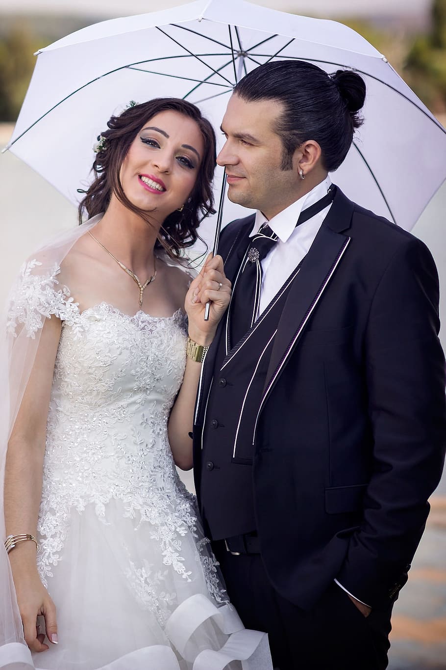 woman in laced white wedding dress standing while holding white umbrella beside man in black suit jacket