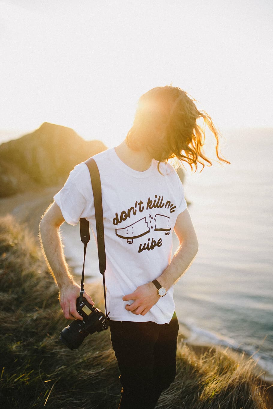 person holding DSLR camera standing on cliff beside body of water during daytime HD wallpaper