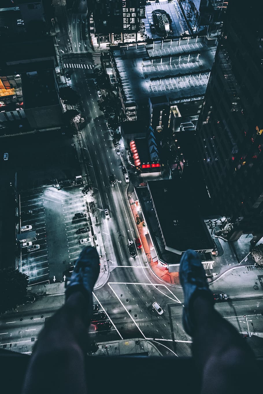 person sitting on top of building, photo of person's leg with view of city during night time