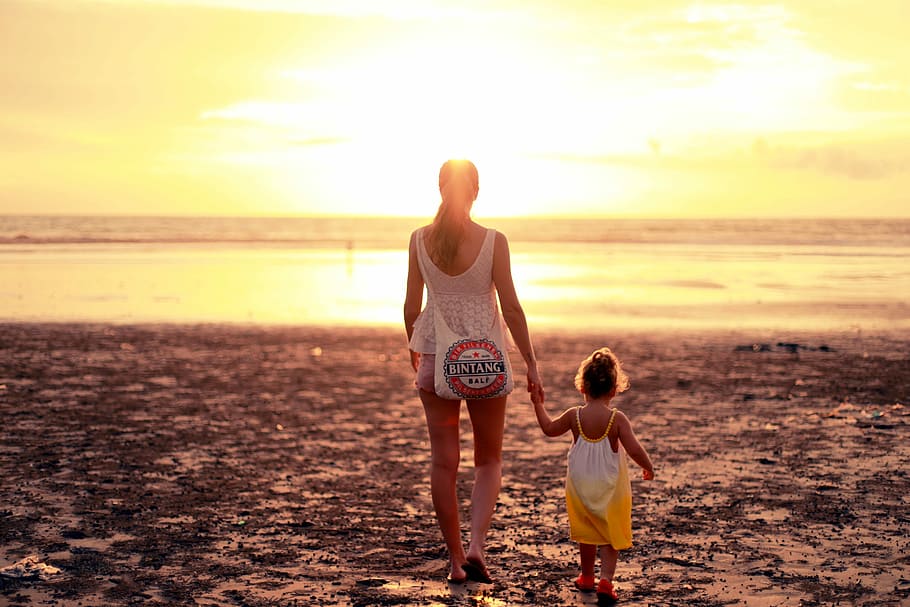 woman and child facing towards sunset, woman holding hand of girl while walking on sand field HD wallpaper