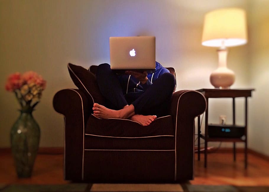 person holding MacBook while sitting on sofa chair, surfing HD wallpaper
