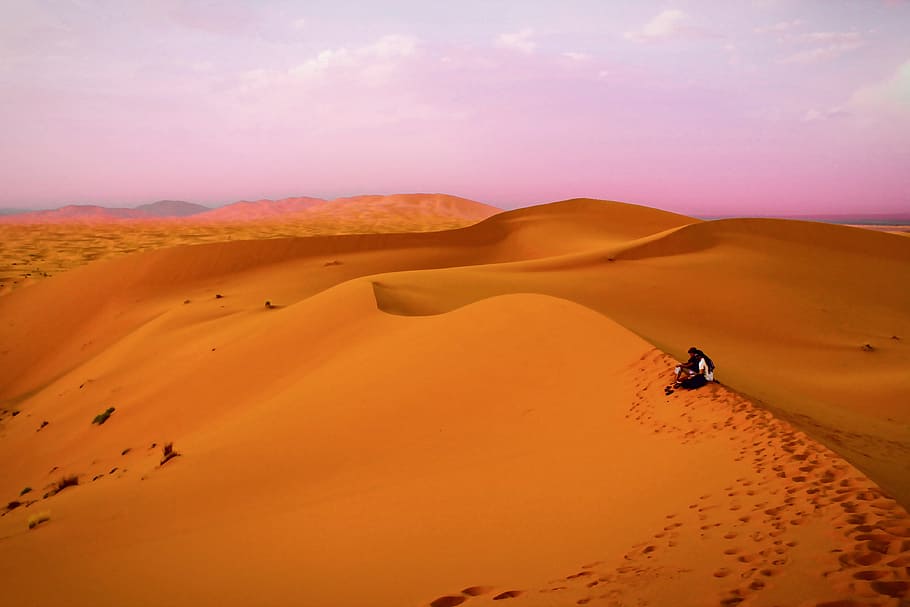 Two people sit in the sandy desert in Morocco, Africa, nature