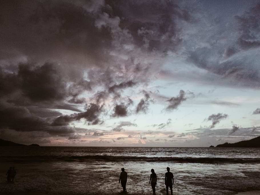 silhouette of three people on seashore under gray cloudy skies, silhouette photography of people at seashore HD wallpaper