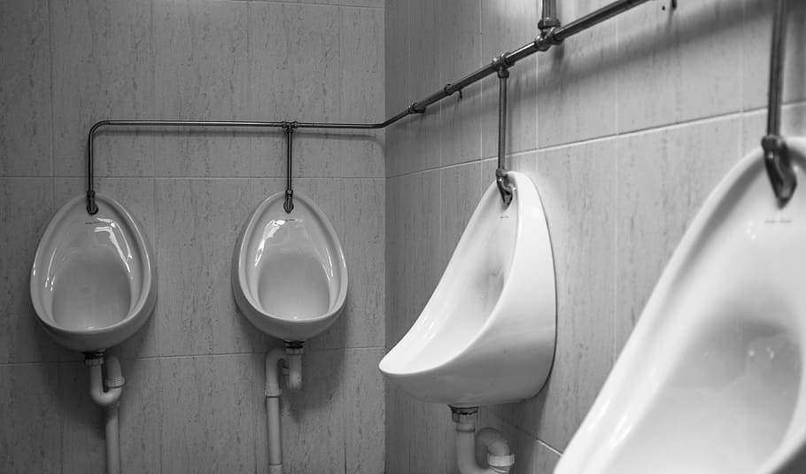 grayscale photography of four white ceramic urinal sinks, white ceramic urinals on wall