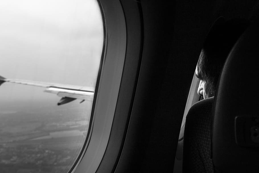 grayscale photo of man sitting near airliner window, grayscale photo of airplane window
