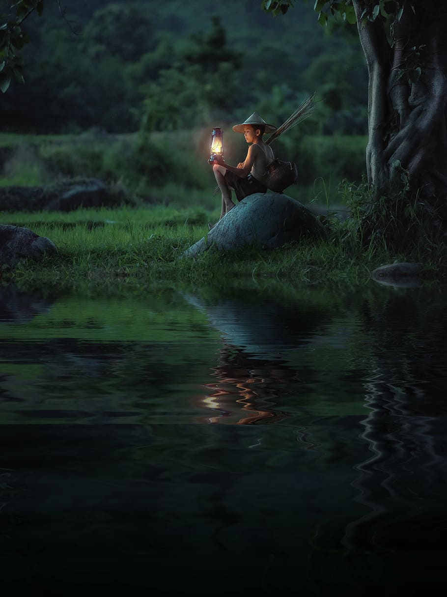 boy holding kerosene lamp sitting on stone near river, background HD wallpaper