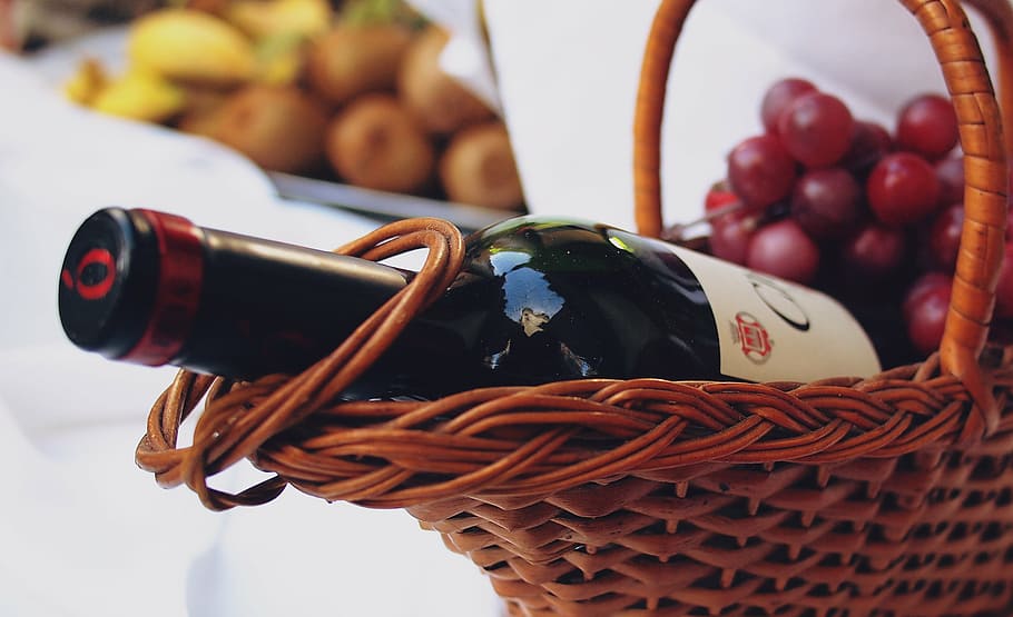close-up photo of wine bottle with grapes on brown wicker basket