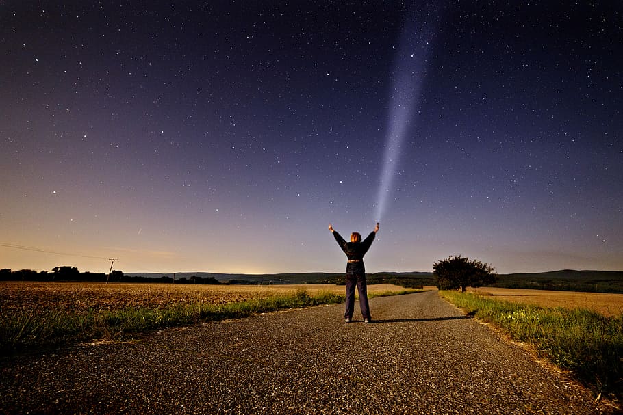 person raising his two hands while holding flashlight standing on road between grass during sunset, person on road raising hands near trees under gray sky HD wallpaper