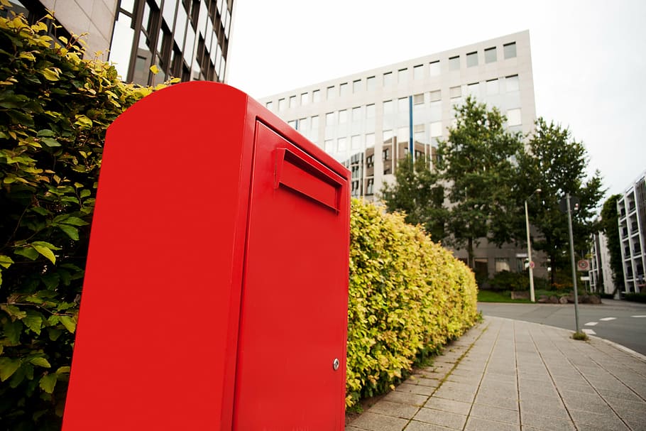 low angle view of red box beside plants and building under gray sky HD wallpaper