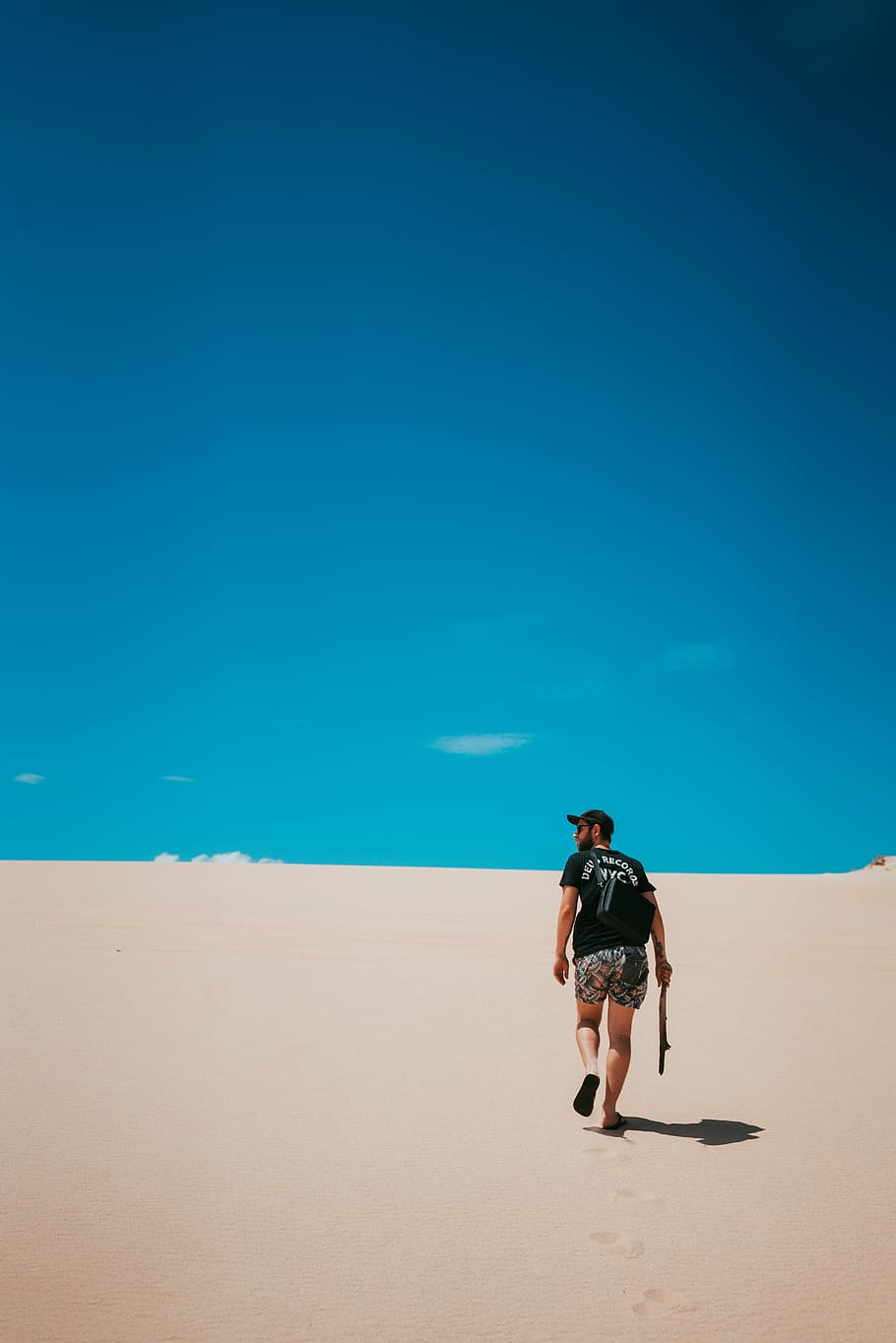 person walking on sand during day time, man walking on desert while holding stick under blue sky HD wallpaper
