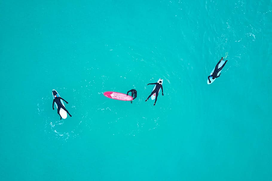 four person on body of water, aerial photography of four people lying and swimming beside surfboards during daytime