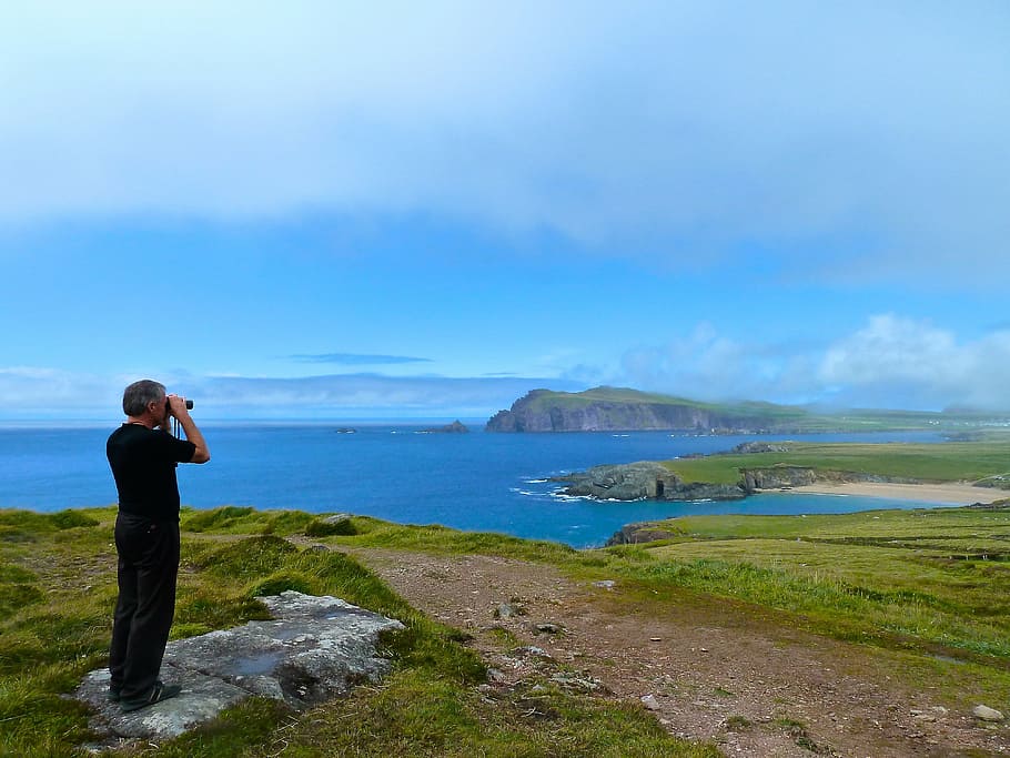 man standing on gray rock formation while using binoculars at daytime HD wallpaper