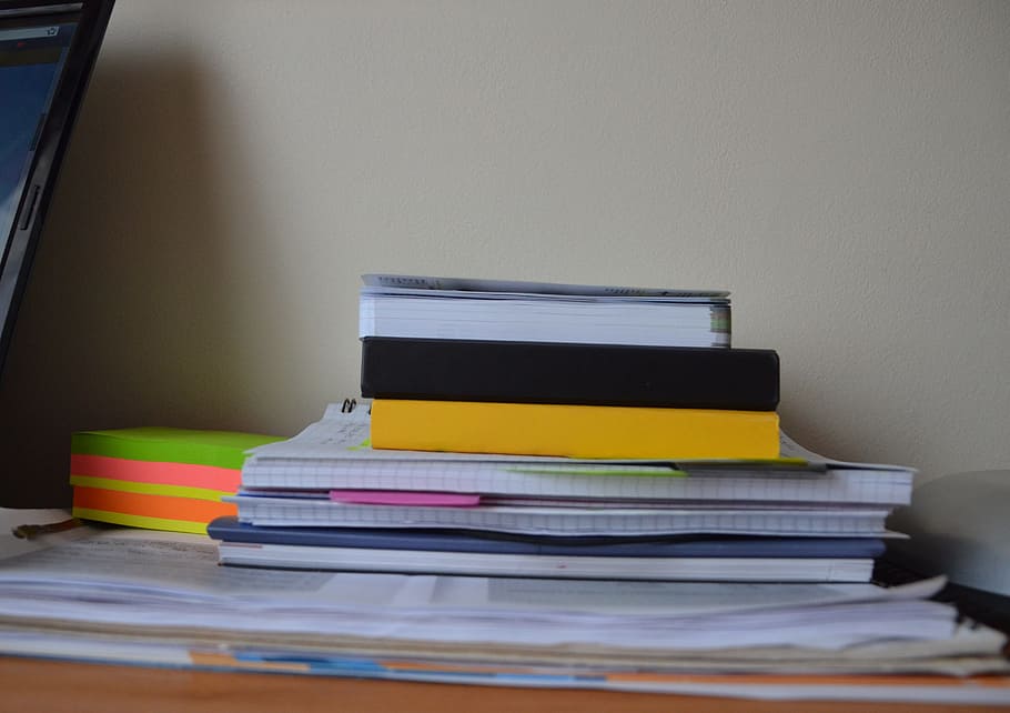 pile of books on the desk with pink paper, papers, supplies, notebooks