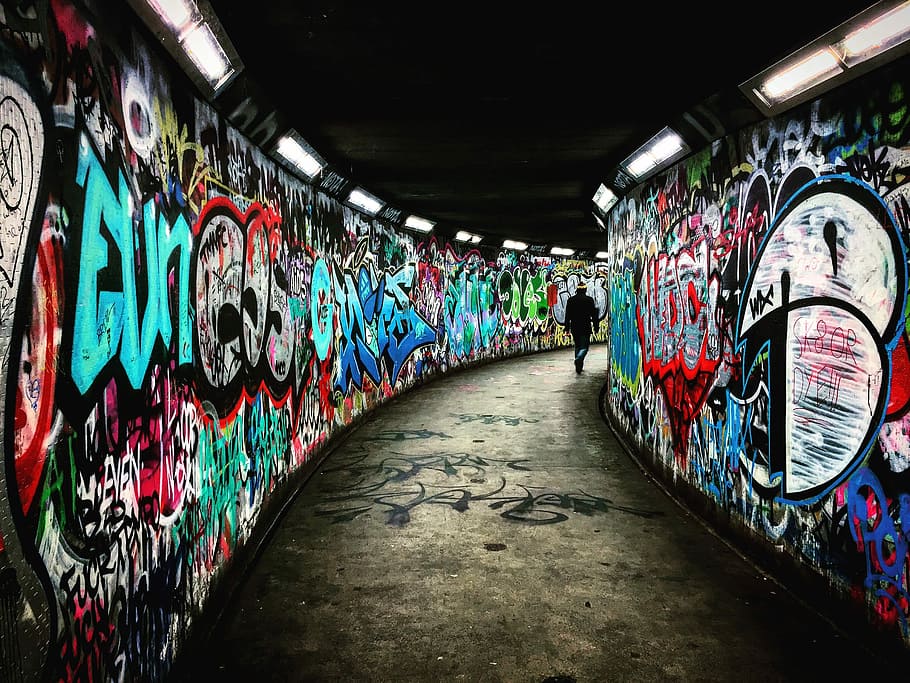 man walking on hallway with graffiti walls, person walking through graffiti tunnel