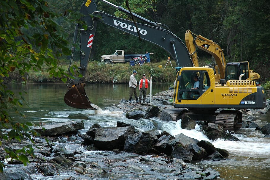 yellow Volvo excavator on rocks near river beside people, equipment HD wallpaper