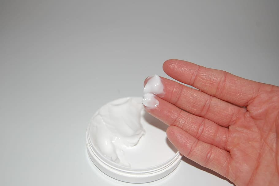 person's hand with white cream near white container, Lubricate