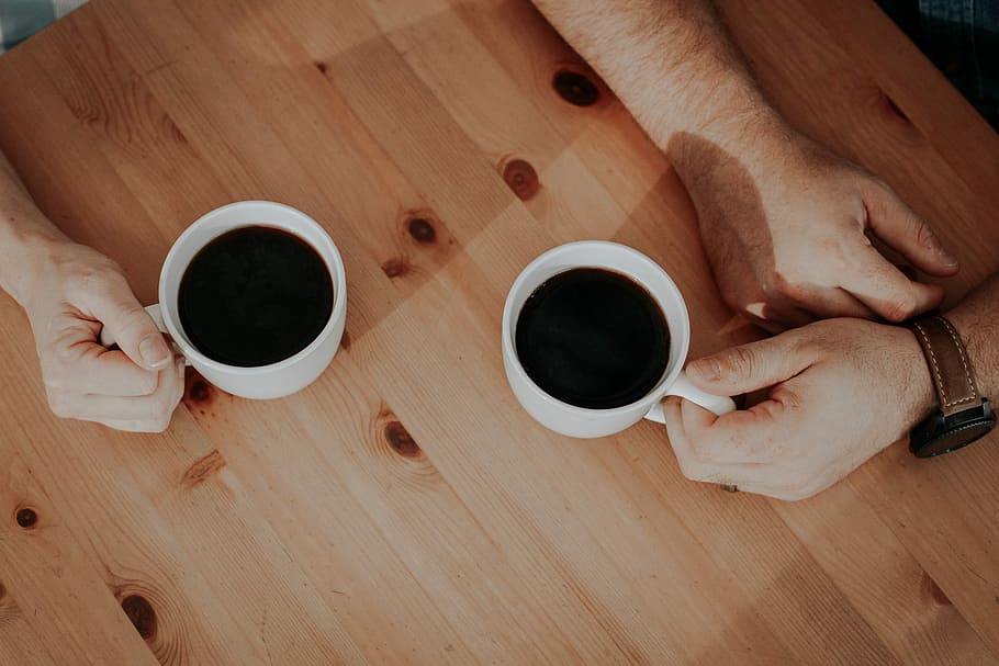 two person holding white mugs filled with coffee's on brown surface, two person's holding white ceramic mugs on brown table HD wallpaper
