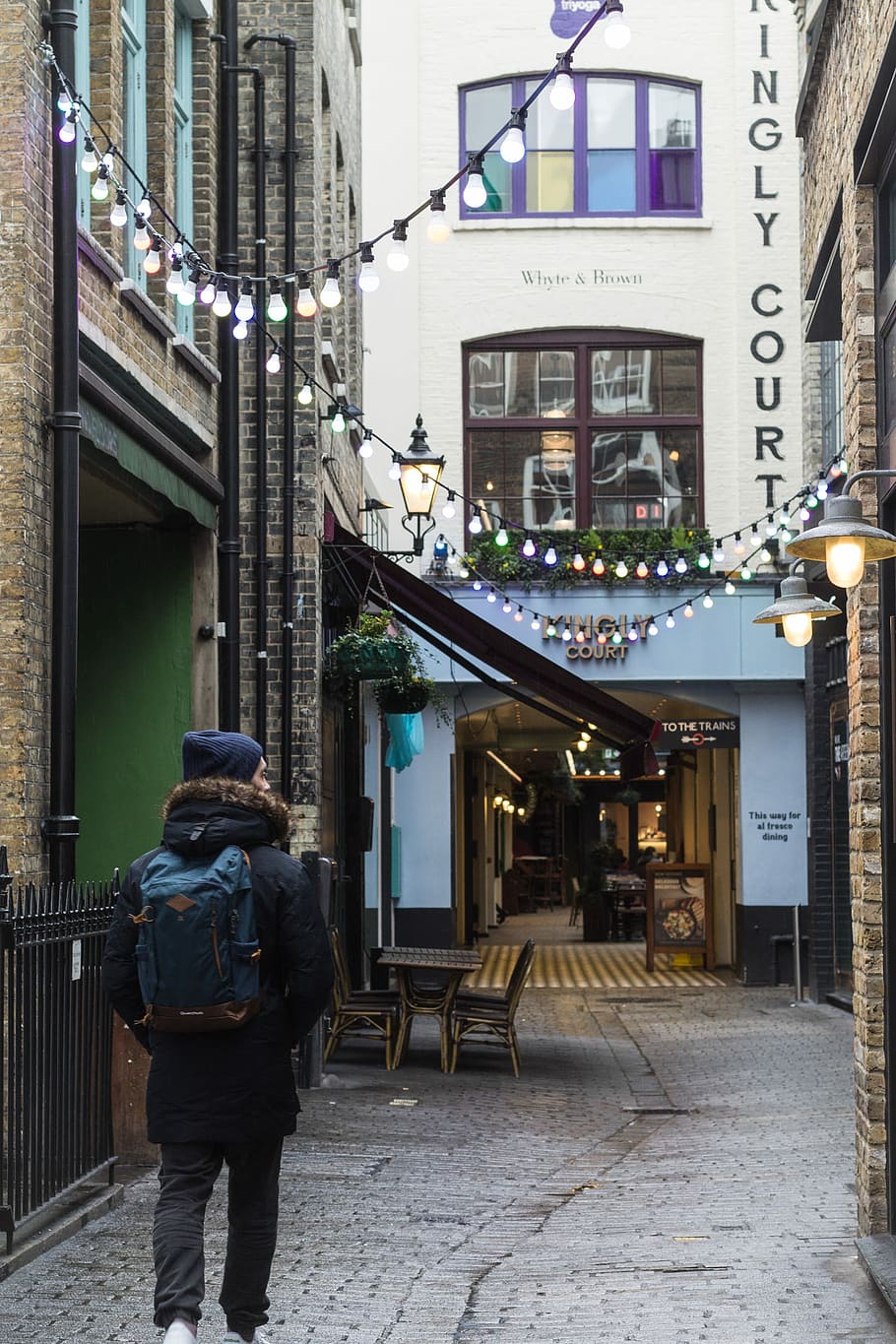 person wearing blue backpack while walking on narrow street, man in black coat and blue backpack walking on gray pavement HD wallpaper