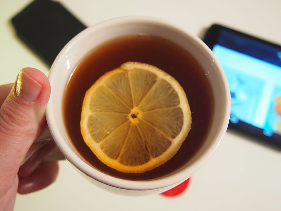 person holding white ceramic cup with tea and sliced lemon HD wallpaper