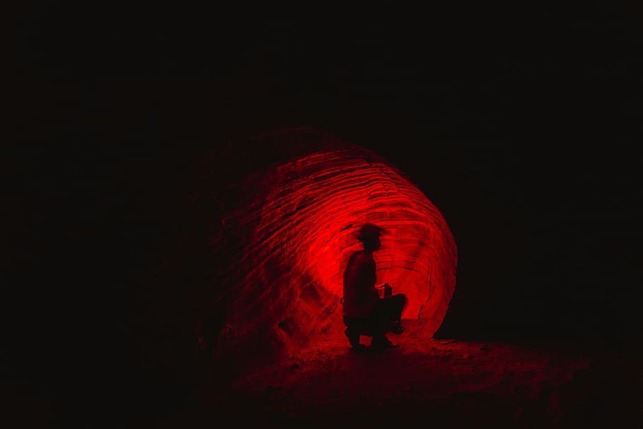 man in cave, silhouette of person sitting near red light, hole