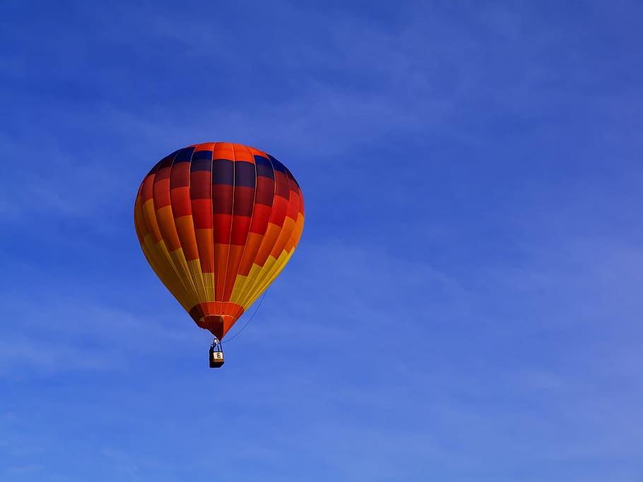 photo of red hot air balloon on sky, blue sky above multicolored hot air balloon on mid air taken at daytime