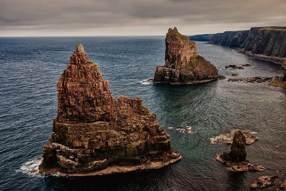 two brown rock formations in sea near cliffs, stacks of duncansby