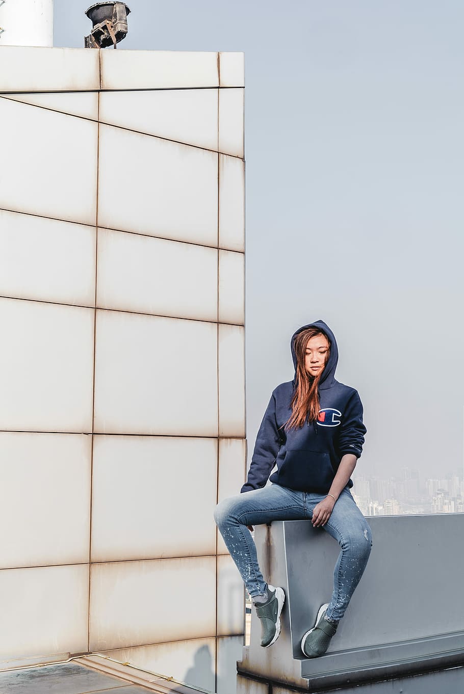 woman sitting on concrete wall on building, woman wearing blue Champion hoodie sitting on wall during daytime, HD wallpaper