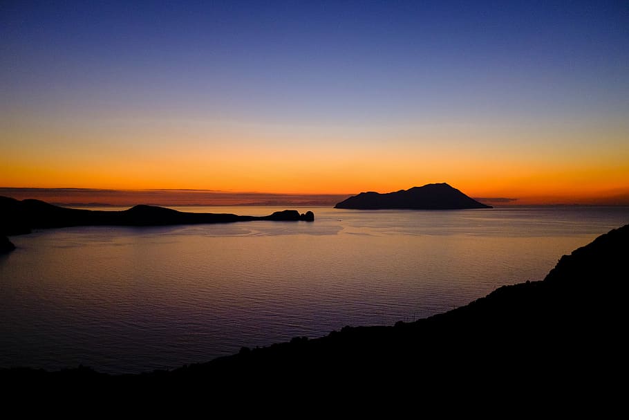 mountains in body of water, calm body of water surrounded by silhouette of mountains during golden hour HD wallpaper