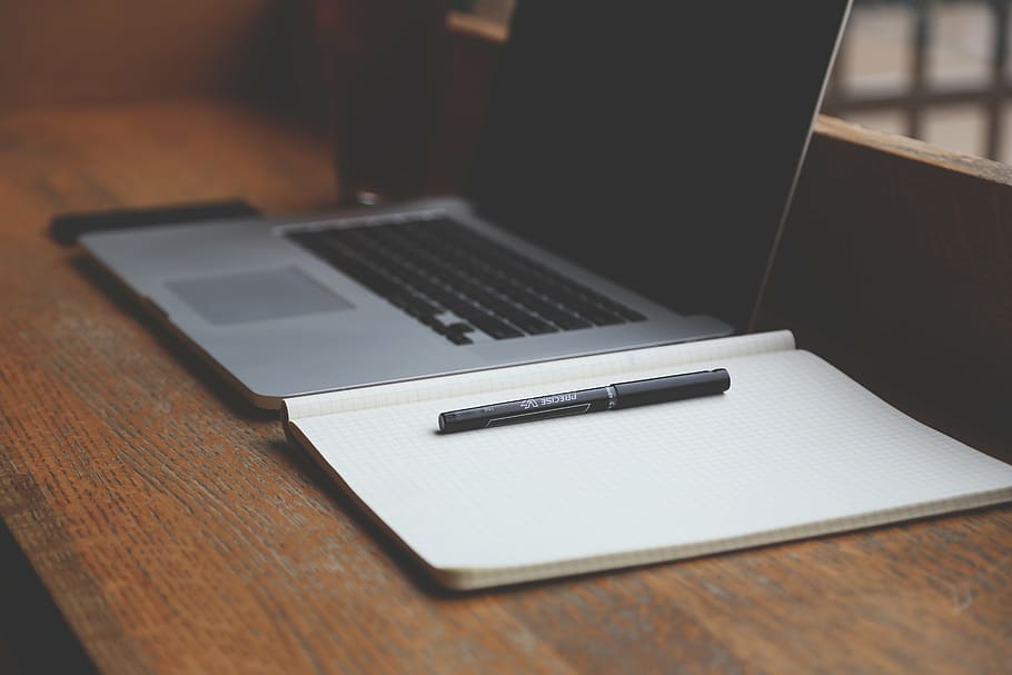 black pen on notebook beside laptop computer on brown wooden table HD wallpaper
