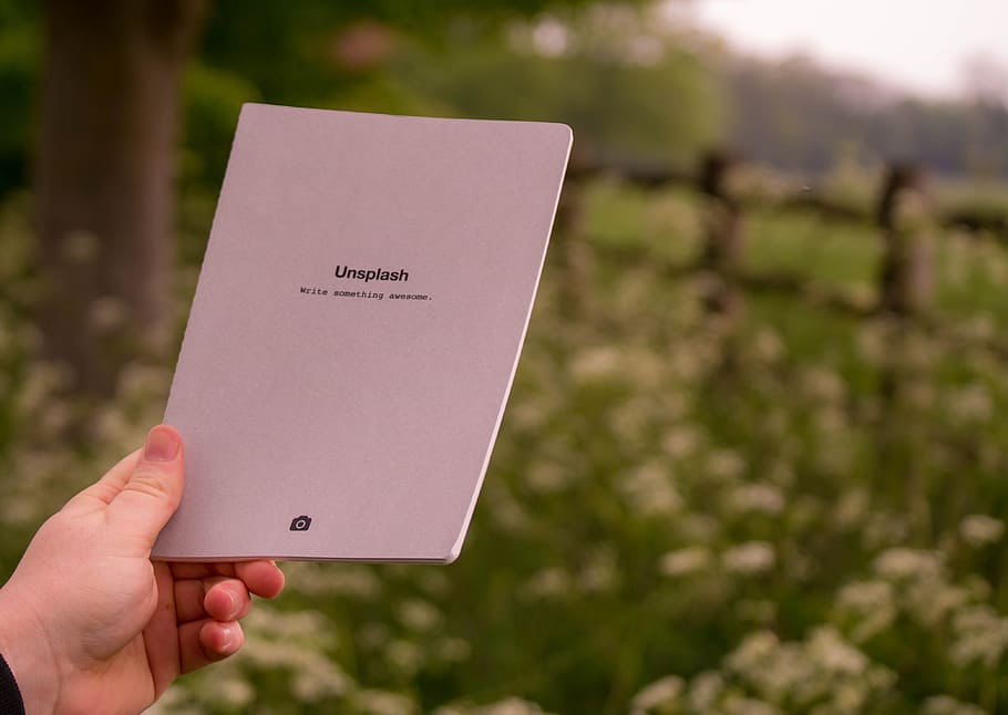 person holding white printer paper, person holding Unsplash book HD wallpaper