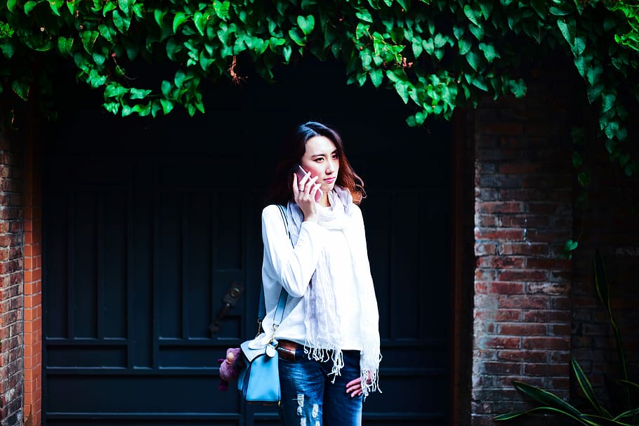 woman standing behind gate while holding phone during daytime, woman holding smartphone in front of the gate HD wallpaper