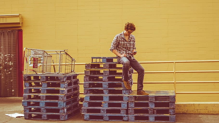 man sitting on top of pallets stack, man sitting on wooden pallets HD wallpaper