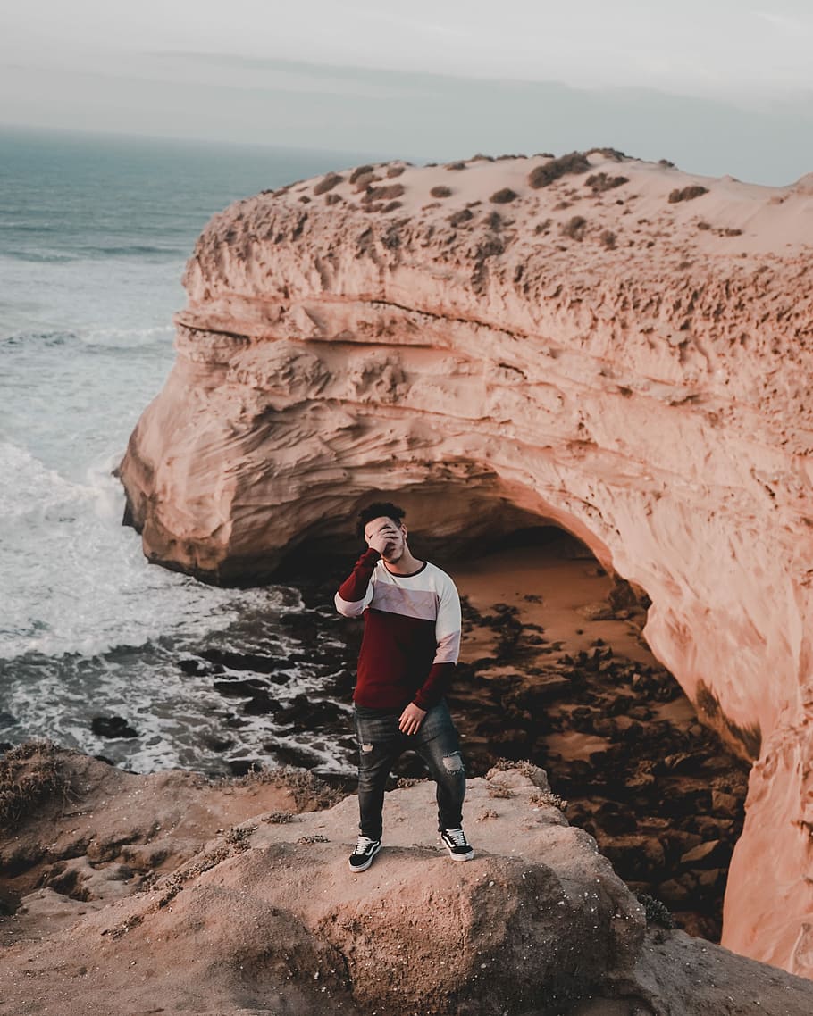 man standing on rock at the shore, man standing on cliff near sea HD wallpaper