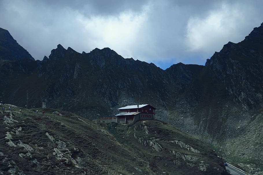 brown house on mountain, white-roofed house behind high mountains under cloudy sky HD wallpaper
