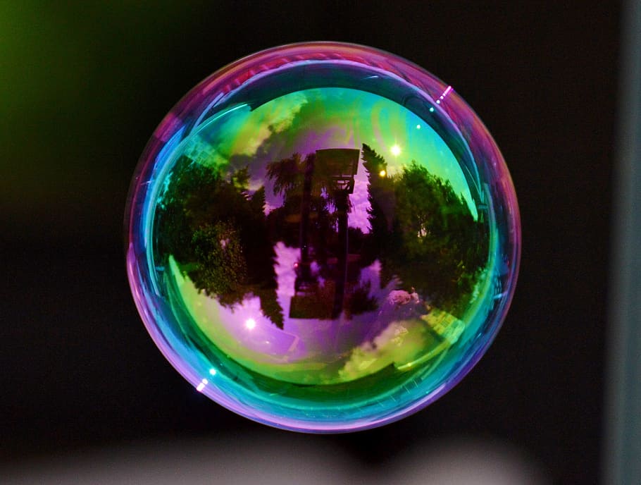 round iridescent bubble showing a reflection of trees, soap bubble