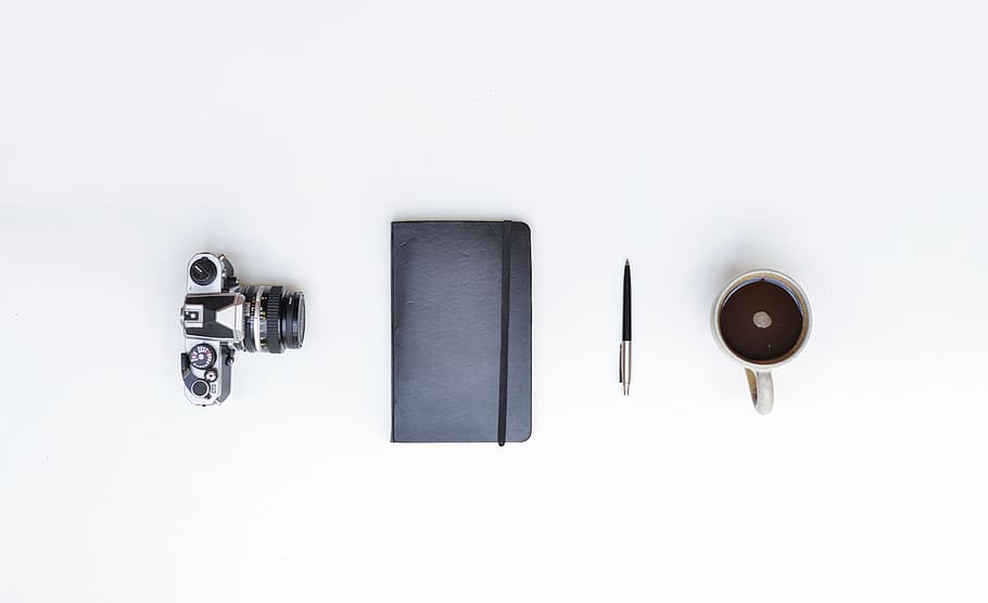 photo of DSLR camera, black handbook, pen, and mug filled with coffee on white surface HD wallpaper
