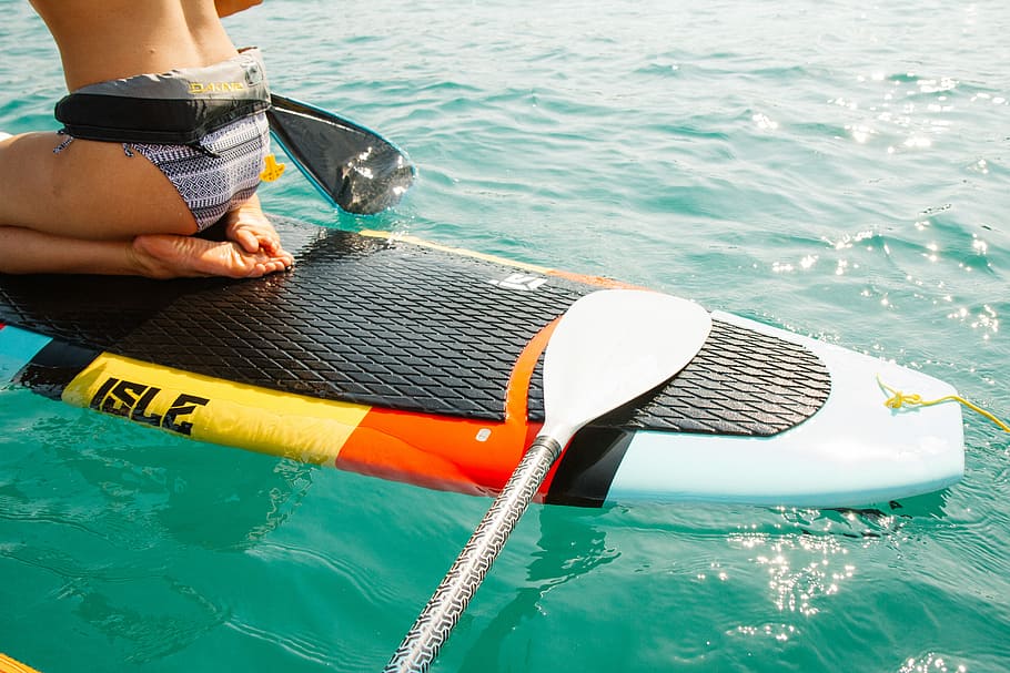 man riding paddle board, woman on white and multicoloired surfboard at daytime HD wallpaper