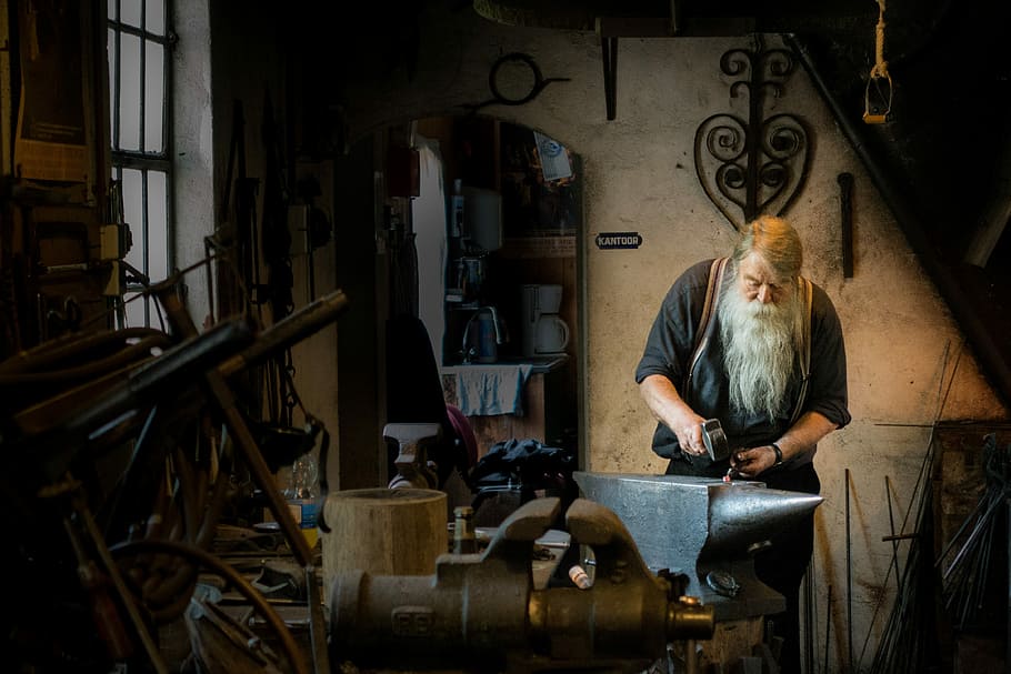 blacksmith holding mallet in garage, blacksmith man holding sledge hammer on anvil