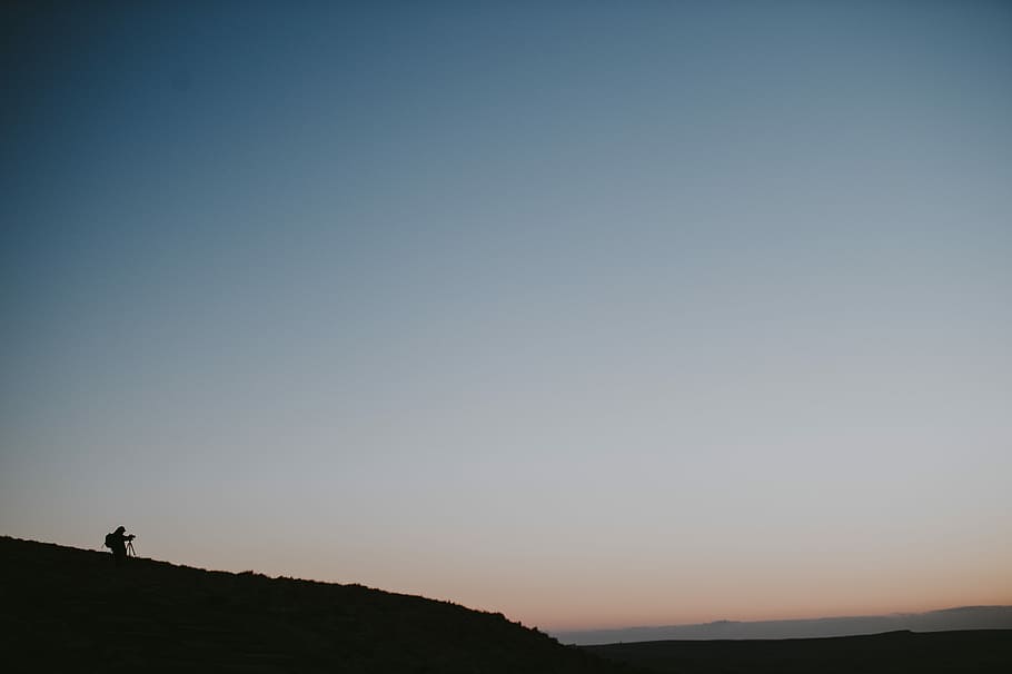 Silhouette of photographer capturing sunrise, person on mountain under white sky HD wallpaper