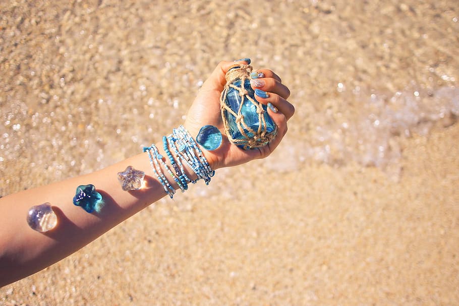 person holding translucent blue glass bottle with assorted accessories on his arm HD wallpaper