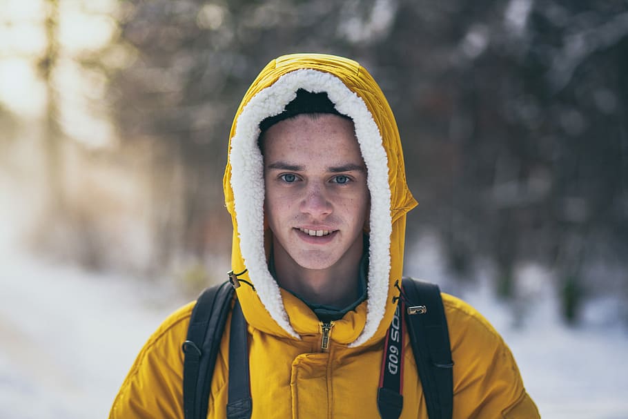 man wearing yellow hooded jacket, man wearing hoodie surrounded by snow