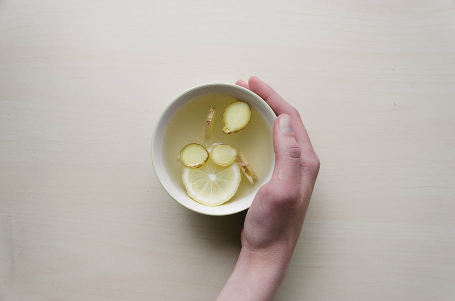 person holding white ceramic cup with sliced ginger and lemon HD wallpaper
