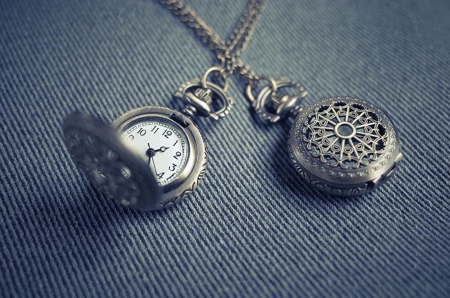 silver-colored stopwatch pendant, closeup photo of two silver-colored pocket watches on blue denim