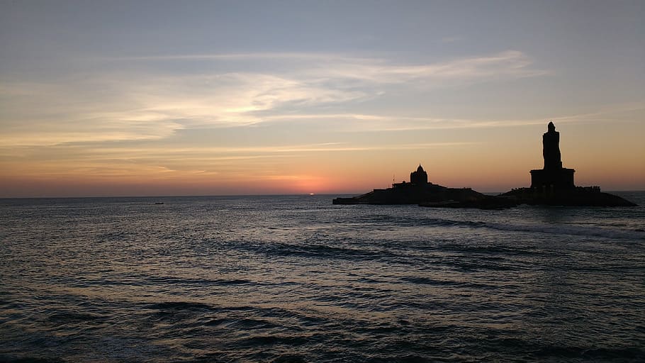 lighthouse beside body of water under calm sky, kanyakumari, sunrise