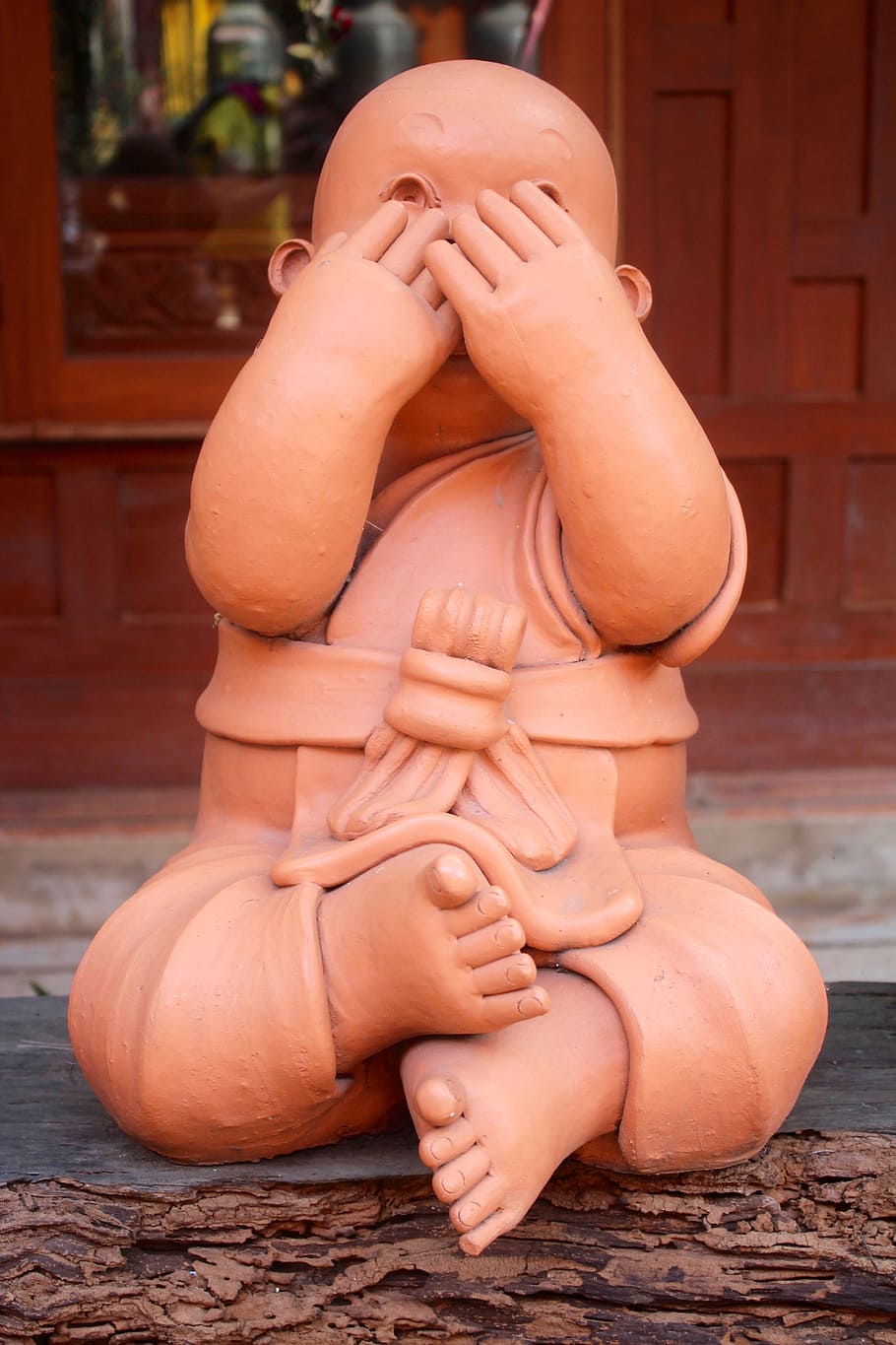 brown ceramic figurine of boy on gray wooden surface, buddha