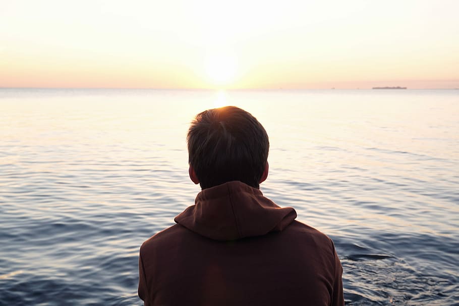 man on body of water, man in brown hooded top facing body of water HD wallpaper
