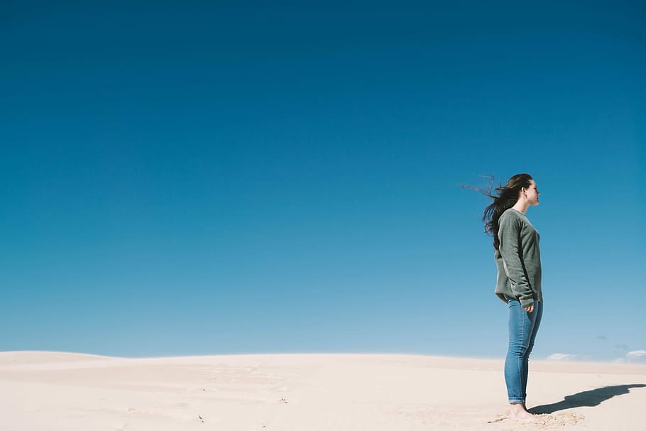 woman standing on gray sand, woman wearing gray sweatshirt and blue jeans standing on brown sand HD wallpaper