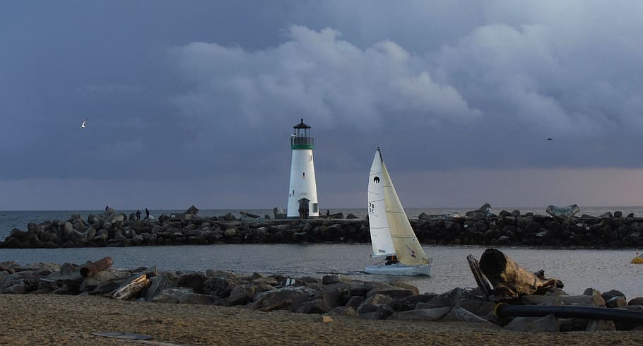 white sailing boat on body of water near black and white lighthouse HD wallpaper